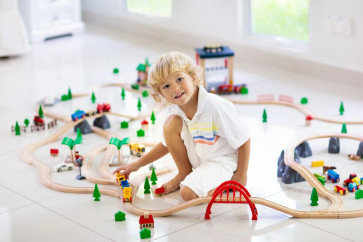 Blond boy sitting on the floor and playing with wooden trains