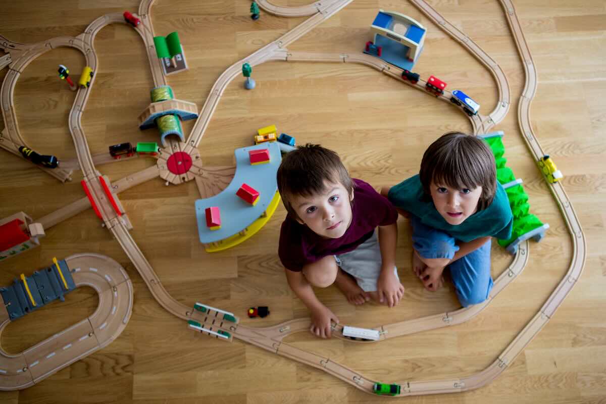 2 boys sitting on the floor amongst a large wooden train set