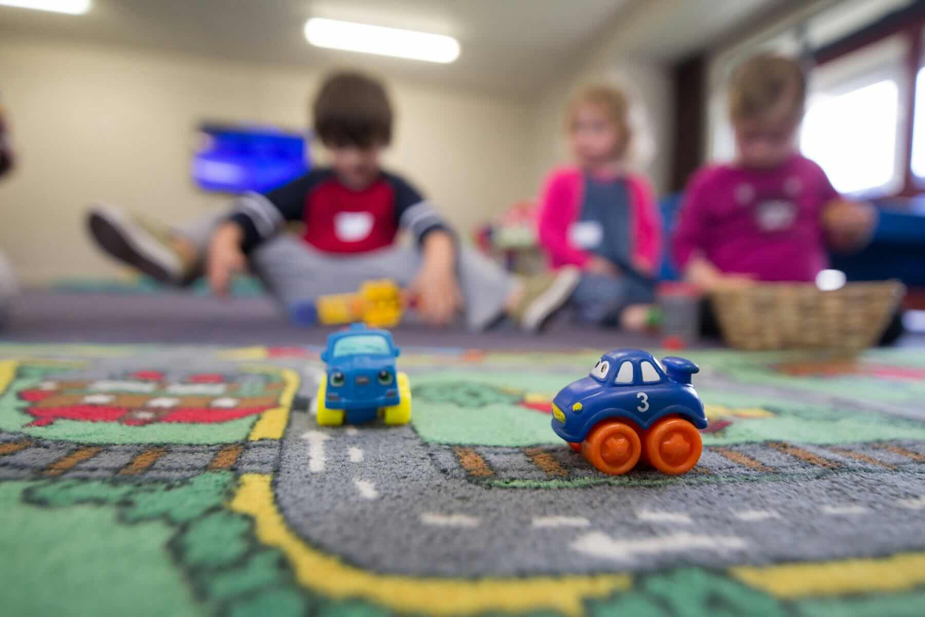 A classroom rug that has roads and train tracks with children seating around it and playing with toy cars