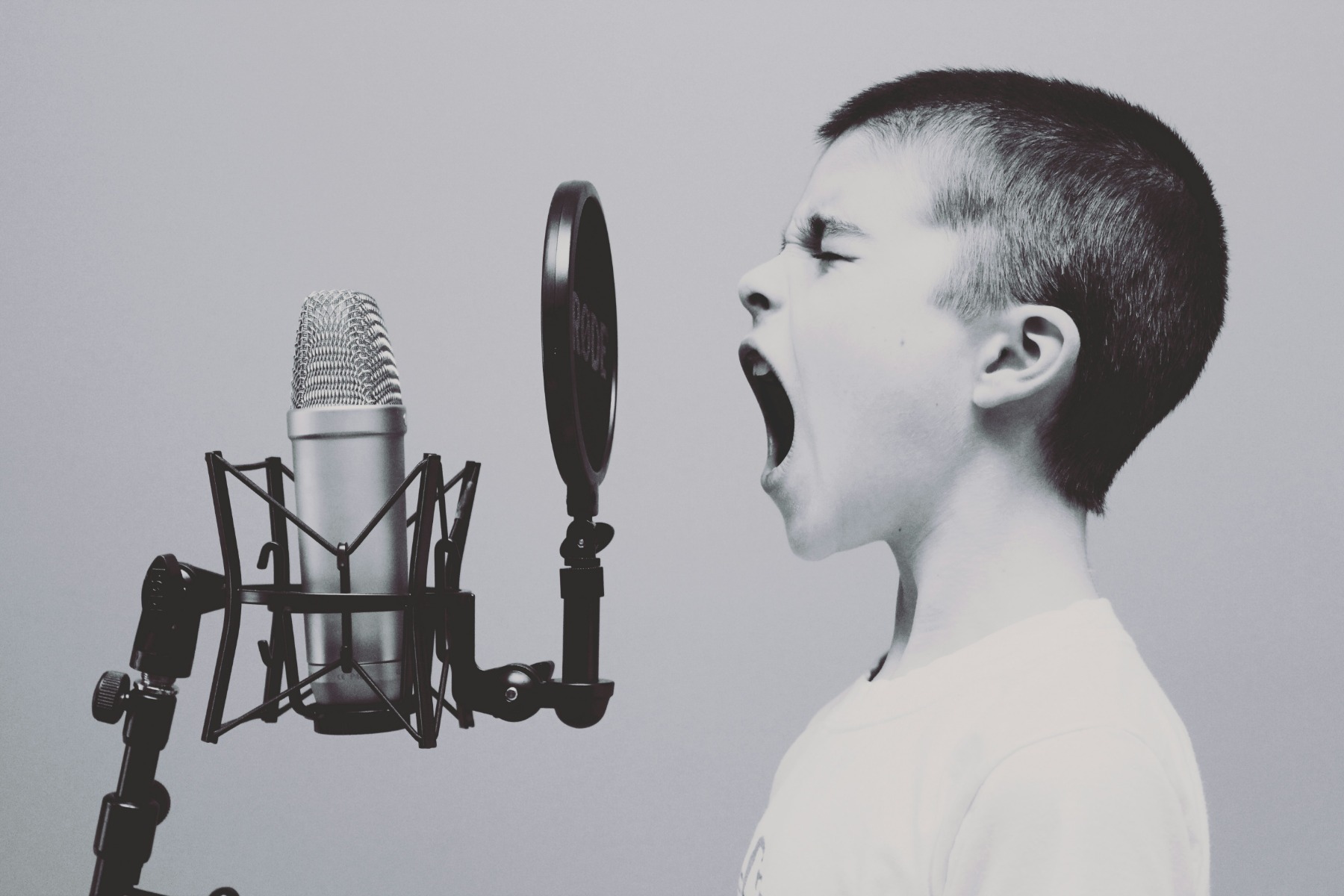 A black and white photograph of a boy shouting into a microphone